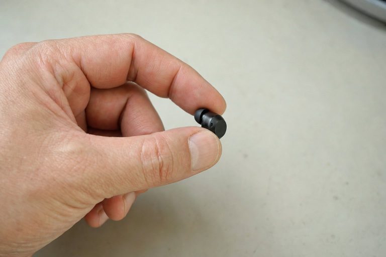 A hand holding a very small wireless earbud to show its size